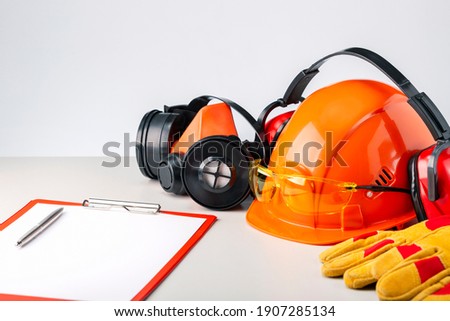 Protective hard hat, headphones, gloves, glasses and clipboard on gray surface.  Construction safety. Royalty-Free Stock Photo #1907285134