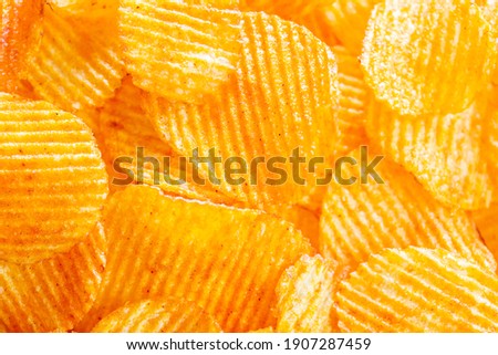 Background of yellow golden grooved fried potato chips with bright lit