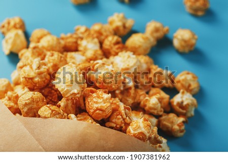 Caramel popcorn in a paper envelope on a blue background. Delicious praise for watching movie movies, serial, cartoon. Free space, close-up. Minimalistic concept.