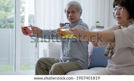 Young older senior asia citizen couple sit on sofa couch with in-home nursing care, assisted living, scrubs nurse use resistance band exercise for senior patient in physiotherapy treatment at home. Royalty-Free Stock Photo #1907401819