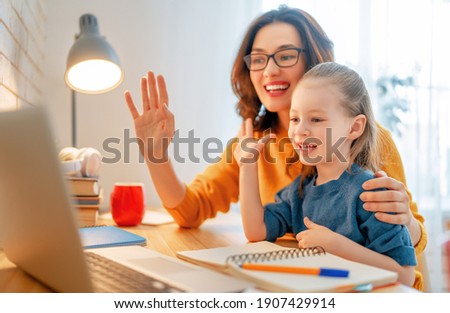 Happy child and adult are sitting at desk. Girl doing homework or online education. Royalty-Free Stock Photo #1907429914