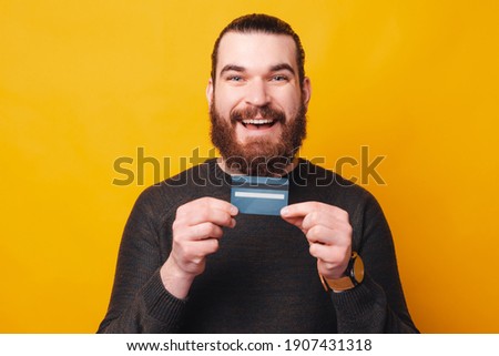 A photo of a bearded man holding a credit card ready to  buy something with it.