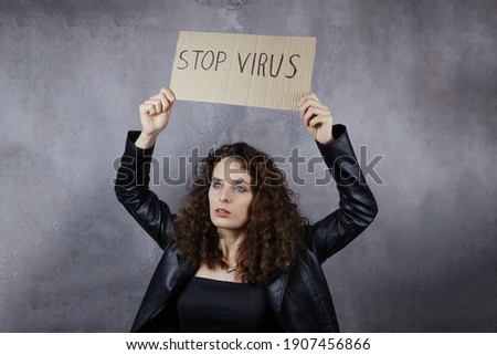 young attractive girl holds a Stop virus poster on a gray background