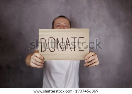 young man holding a board with text Donate. Selective focus