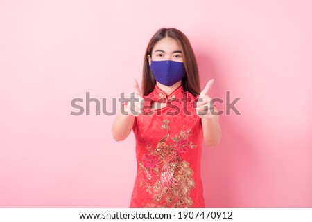 Portrait Asian Young Women and wear face mask protect Wearing red cheongsam , isolated on pink background. Flu epidemic, dust allergy, protection against virus. protection concept