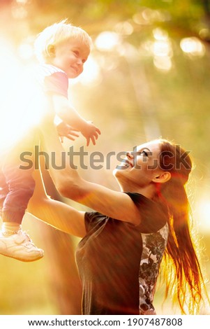 Young mother holds her son. Woman is having fun with her little baby in a summer park. Happy mom throws up child while playing outdoors