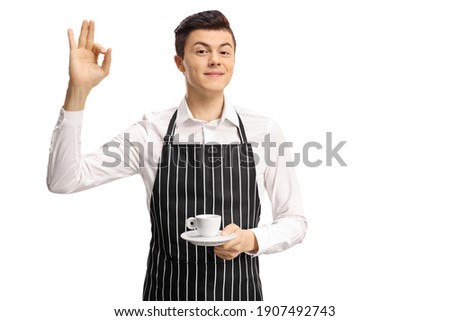 Young waiter holding an espresso coffee and gesturing ok sign isolated on white background