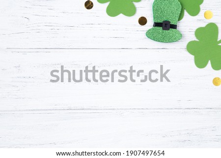 Patricks day background with copy space. Green clover leaves and hat with golden glitters on the white wooden table, border.