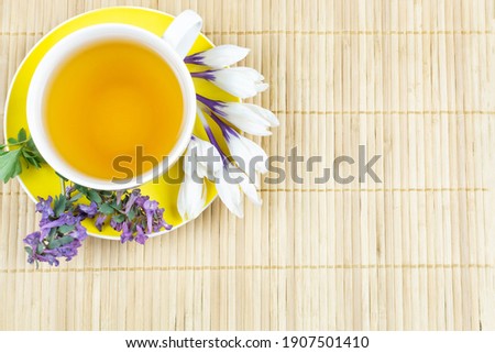 A cup of tea in a yellow mug on a saucer and spring flowers snowdrops and tufts on a bamboo background. Space for the text. Good morning. The concept of the holiday.