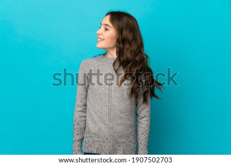 Little caucasian girl isolated on blue background looking to the side and smiling