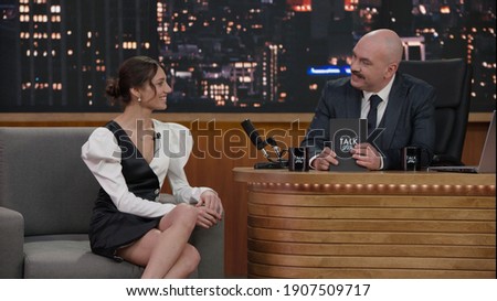 Late-night talk show host having a conversation with celebrity guest in a studio. TV broadcast style show Royalty-Free Stock Photo #1907509717