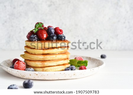 Pancakes with berries and maple syrup for breakfast on a light background. Royalty-Free Stock Photo #1907509783