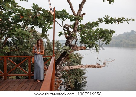 Pretty young woman stand near the lake or river and use mobile phone, texting message