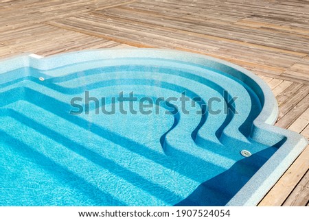 New modern fiberglass plastic swimming pool entrance step with clean fresh refreshing blue water on bright hot summer day at yard or resort hotel spa area. Wooden flooring deck of teak or larch board Royalty-Free Stock Photo #1907524054