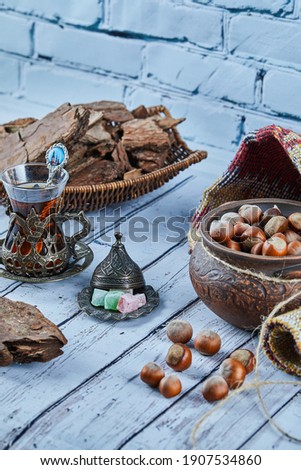 Black tea in a traditional glass cup with candies and a bowl of hazelnuts on blue wooden table