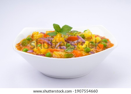 Mixed veg curry or kurma  tasty indian dish made of vegetables like cauliflower, carrot, potato, green peas and garnished with onion pieces and mint leaf placed in a white ceramic bowl with background Royalty-Free Stock Photo #1907554660