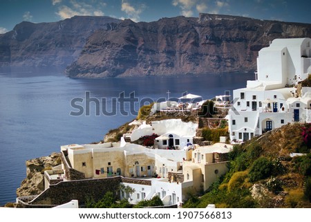 Santorini, Greece: Wide angle aerial shot of cityscape showing White houses built on mountain against beach and mountains during summer