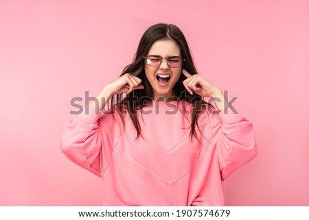 Photo of attractive young woman in glasses too noisy scream. Wears casual pink t-shirt white pants isolated pink color background