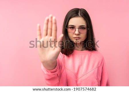 Photo of attractive young woman in glasses gesture stop, wears casual pink t-shirt white pants isolated pink color background
