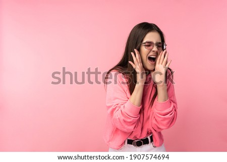 Photo of attractive young woman in glasses scream and yelling loudly, wear casual pink t-shirt white pants isolated pink color background