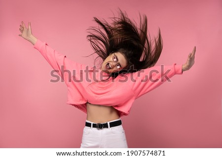 Photo of attractive young woman in glasses has fun dance with music, wears casual pink t-shirt white pants isolated pink color background
