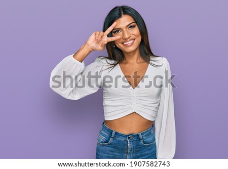 Young latin transsexual transgender woman wearing casual clothes doing peace symbol with fingers over face, smiling cheerful showing victory 