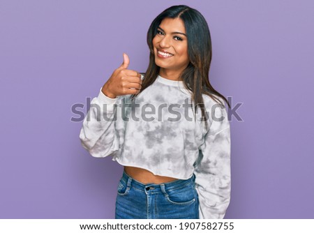 Young latin transsexual transgender woman wearing casual clothes doing happy thumbs up gesture with hand. approving expression looking at the camera showing success. 