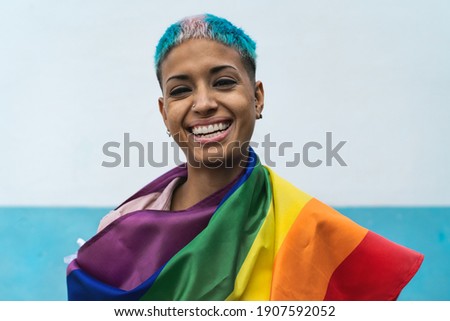 Young activist woman smiling and  holding rainbow flag symbol of Lgbtq social movement Royalty-Free Stock Photo #1907592052