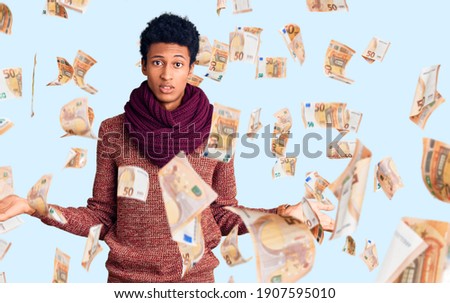 Young african american man wearing casual winter sweater and scarf clueless and confused with open arms, no idea concept.