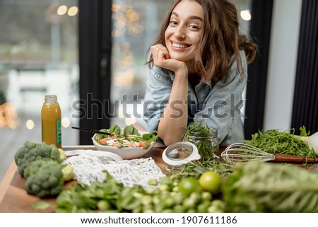 Young pretty woman smiling and eating healthy diet salad and smoothie in the kitchen. Wellness and health care concept. Looking at camera. High quality photo