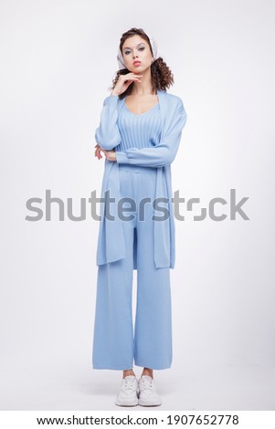 High fashion photo of a beautiful elegant young woman in a pretty blue suit, pants, top, cardigan, sneakers, head scarf posing over white background. Studio Shot. Portrait