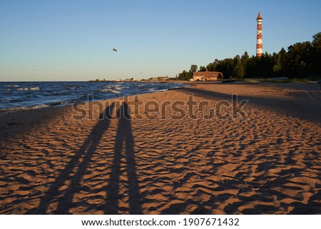 People are making photograph of their shadow at the sandy beach with lighthouse.
