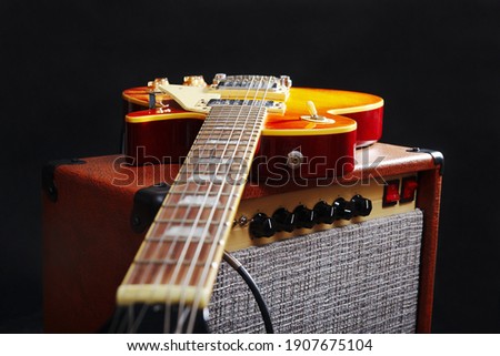 Brown amplifier for electric guitar with honey sunburst guitar on the black background. 