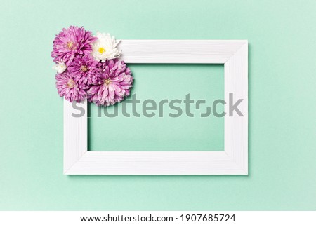 Flowers composition. Empty photo frame and flowers on pastel green background. Valentines day, mothers day, womens day, spring concept. Flat lay, top view, copy space.