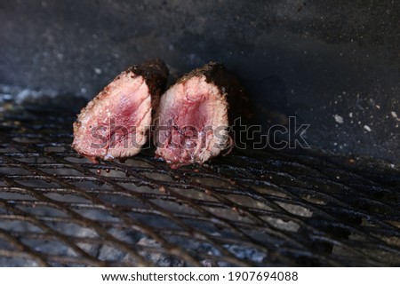 Medium rare ostrich steaks being cooked on a braai grid. This photo has selective focus. 