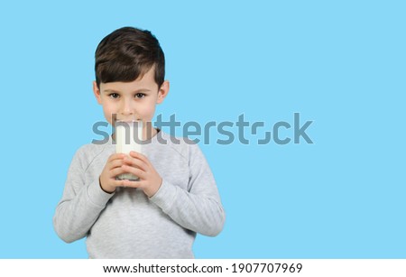 Boy in a gray sweater holds a glass of milk on blue isolated background.A child  drinks milk. Dairy products for children, copy space