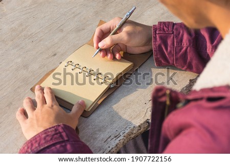 A close-up picture of a man in a red dress writing on a wooden table