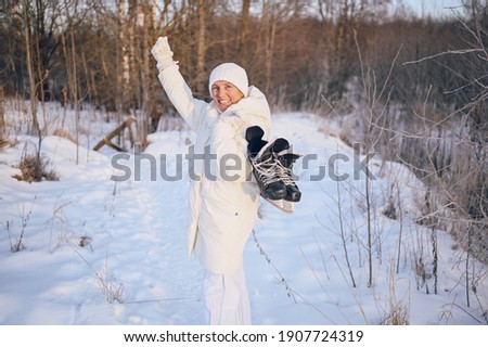 Happy elderly senior mature woman in white warm outwear playing with ice skates in sunny snowy winter outdoors. Retired healthy people holiday vacation winter activities, active lifestyle concept