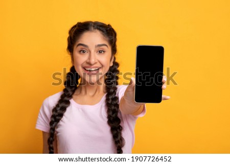 Trendy Mobile Phone. Portrait of cheerful young indian woman holding cellphone with black blank screen in hand, showing device. Gadget with empty free space for mock up, selective focus, blur Royalty-Free Stock Photo #1907726452