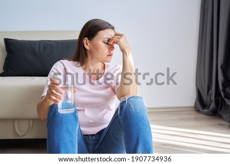 Depression, neurosis, fears, stress, mental health problems, the consequences of the disease coronavirus covid-19. Sad unhappy mature woman sitting at home on floor with glass of water Royalty-Free Stock Photo #1907734936