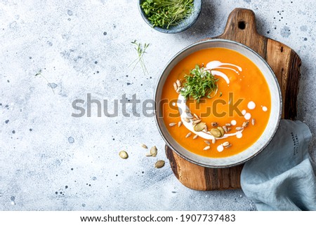 Vegetarian autumn pumpkin and carrot soup with cream, seeds and cilantro micro greens. Comfort food, fall and winter healthy slow food concept