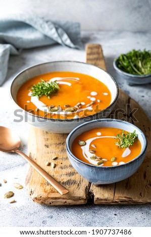 Vegetarian autumn pumpkin and carrot soup with cream, seeds and cilantro micro greens. Comfort food, fall and winter healthy slow food concept Royalty-Free Stock Photo #1907737486