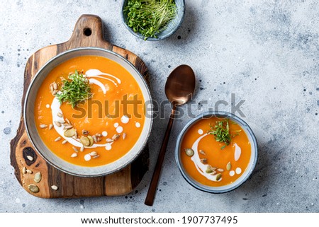 Vegetarian autumn pumpkin and carrot soup with cream, seeds and cilantro micro greens. Comfort food, fall and winter healthy slow food concept