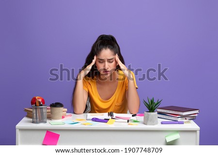 Portrait of fatigue tired indian lady feeling headache or stress, touching and massaging her temples, trying to learn and study, sitting at desk with notebook. Woman doing homework and thinking Royalty-Free Stock Photo #1907748709