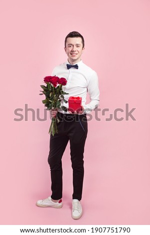 Valentines day. Handsome smiing boy holding flowers and gift box on pink background.