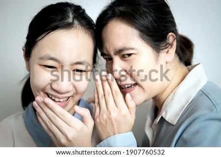 Asian mother whispering gossiping in her daughter ear,adult woman look at other with disdain,aversion,telling a secret to slandering others to teen girl,facial expression of disapproval or irritation Royalty-Free Stock Photo #1907760532