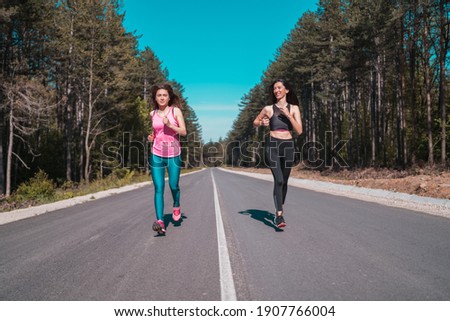 Slim athletic joggers in sports leggins run along the road in beautiful green forest.