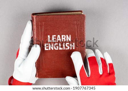 Learn English concept. Leather work gloves in hand and a textbook on a gray background. 