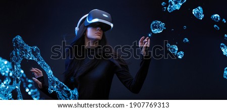 Beautiful woman with flowing hair over dark magic background. Girl in glasses of virtual reality while touching air in blue neon lights. Augmented reality, game, future technology concept. VR. Royalty-Free Stock Photo #1907769313