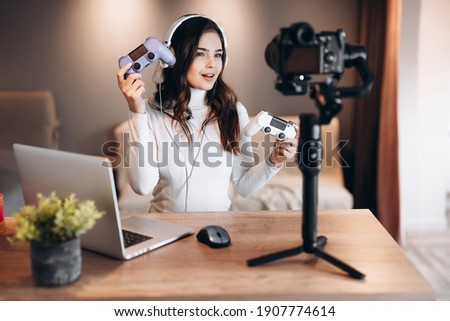 Beautiful blogger woman in headphones is streaming live talking about video games. Influencer young woman is having fun live streaming with laptop indoor Royalty-Free Stock Photo #1907774614